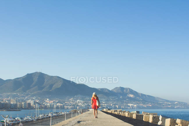 Frau mit rotem Kleid und Hut geht die Seebrücke hinunter — Stockfoto