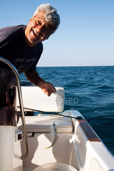 Happy Fisherman standing on boat in sea with fresh caught fish — Stock Photo