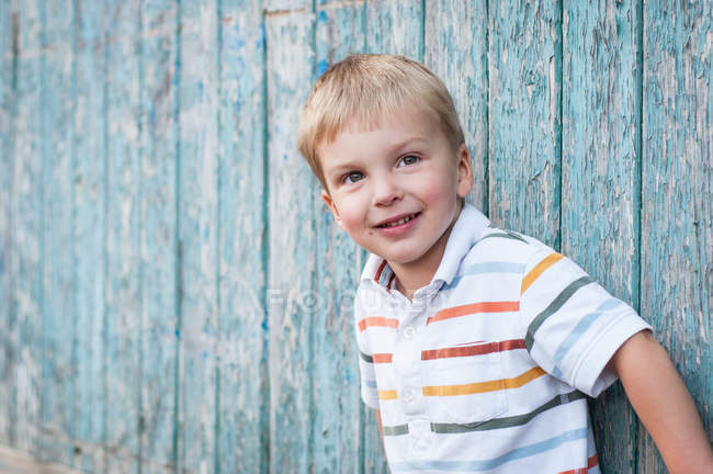 Portrait de garçon souriant debout contre un mur en bois minable — Photo de stock