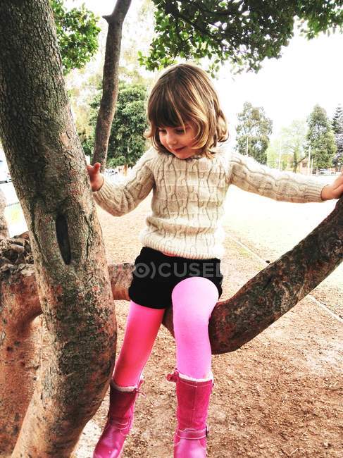 Niña vistiendo botas rosas trepando árbol - foto de stock