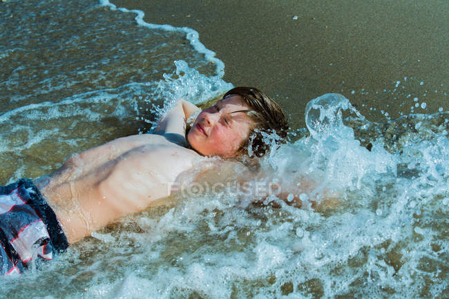 Мальчик лежит в серфинге на песчаном пляже — стоковое фото