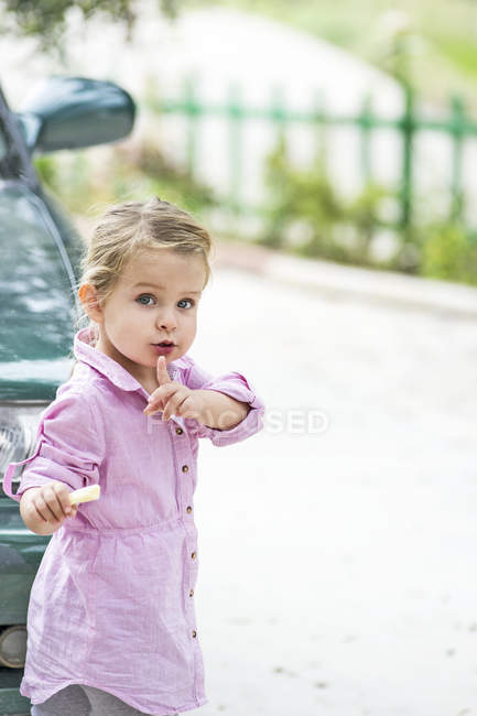 Portrait of beautiful little girl standing near car and gesturing for silence — Stock Photo