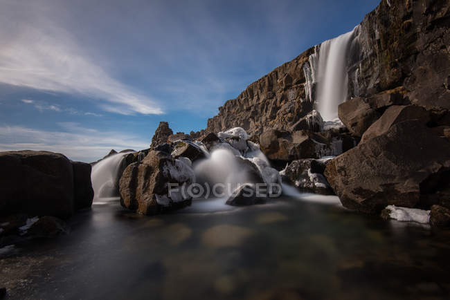Iceland, Azingvellir National Park, Rock formation with waterfall shot with long exposure — Stock Photo