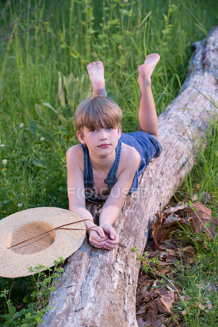 Young boy wearing blue overalls laying on fallen tree — Stock Photo