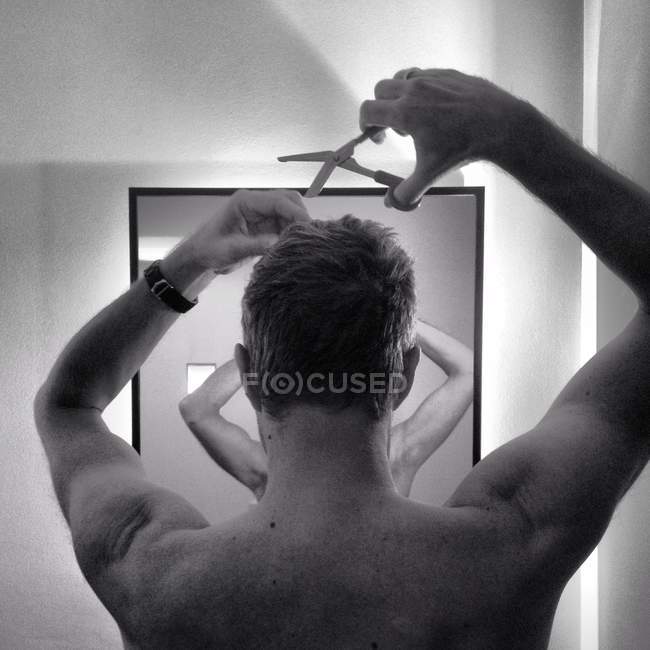 Homme torse nu coupant les cheveux devant le miroir — Photo de stock
