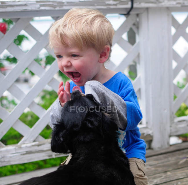 Портрет хихикающего мальчика, играющего с собакой — стоковое фото
