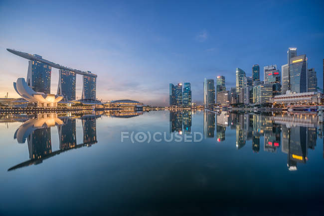 Singapore, Waterfront skyscrapers reflecting in still harbor in evening — Stock Photo