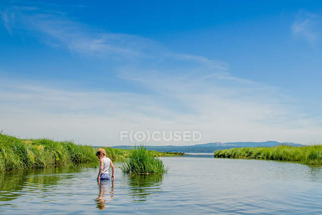 Маленький мальчик стоит в озере с облачным небом на заднем плане — стоковое фото