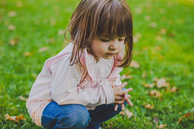 Portrait of little girl crouching on grass — Stock Photo