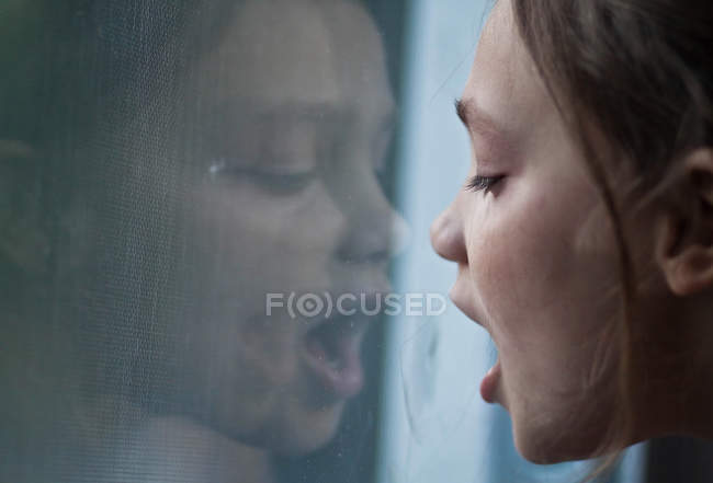 Primo piano di carina bambina che respira sulla finestra con riflesso — Foto stock