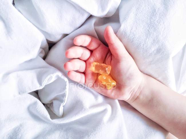 Abgeschnittenes Bild von Kleinkind, das Teddybär-Weingummis über dem Bett hält — Stockfoto
