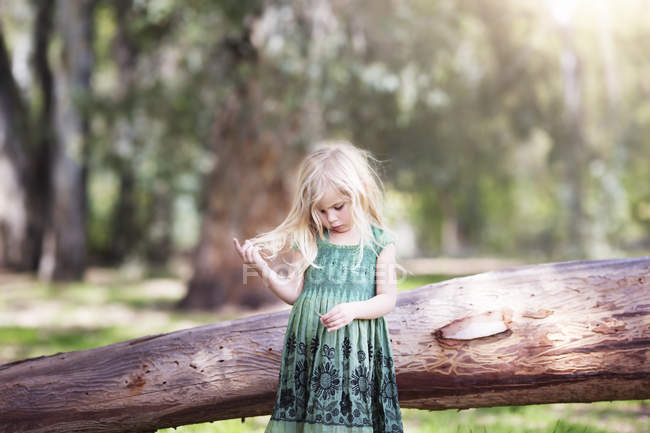Блондинка в зеленом платье играет с волосами в лесу — стоковое фото