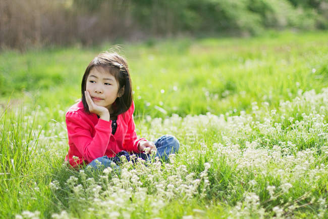 Menina sentada em um campo e descansando o queixo na mão — Fotografia de Stock