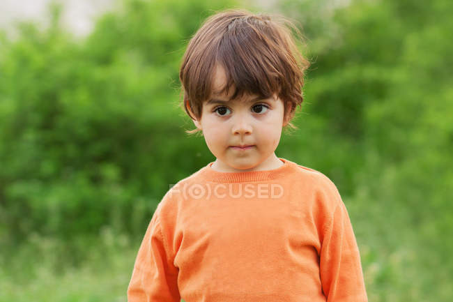 Daydreaming menino vestindo laranja jumper de pé ao ar livre — Fotografia de Stock