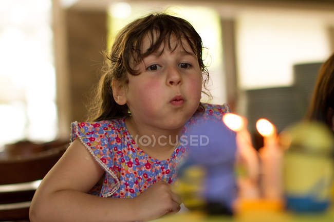 Portrait of girl blowing out candles on blurred background — Stock Photo