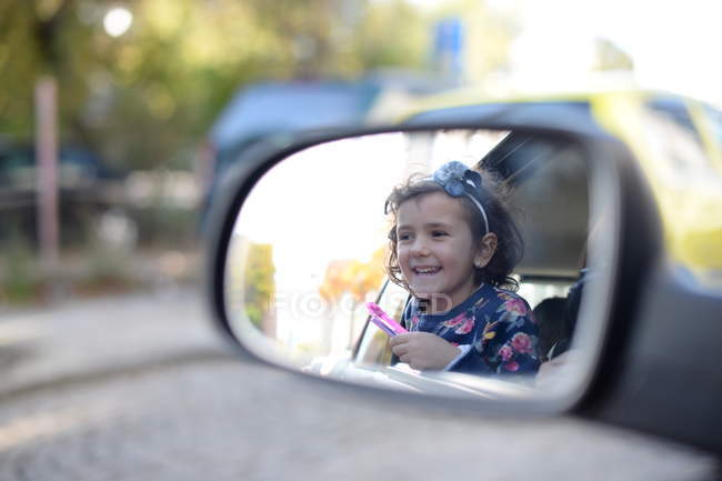 Маленькая девочка наслаждается поездкой на машине и смотрит в зеркало заднего вида — стоковое фото
