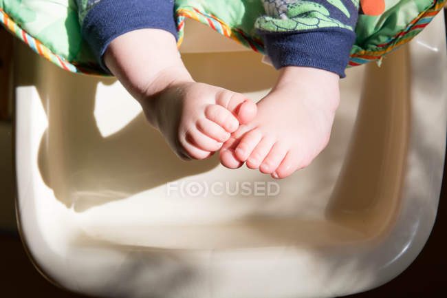 Imagen recortada de pies de bebé en silla alta en la luz de la mañana - foto de stock