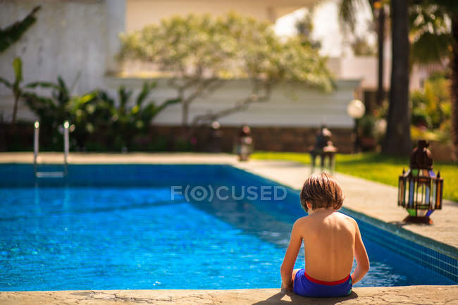 Хлопчик сидить на краю басейну влітку — стокове фото