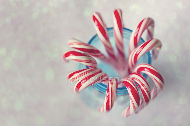 Red and white striped candy canes in blue mason jar against glittering background — Stock Photo