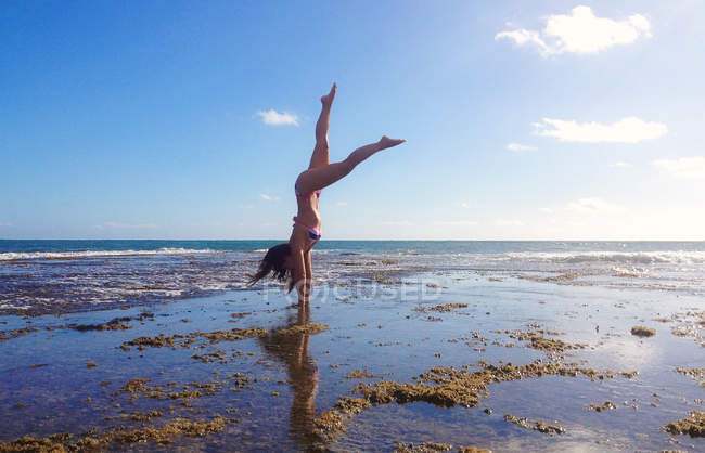 Frau macht Handstand am Strand vor blauem Himmel — Stockfoto