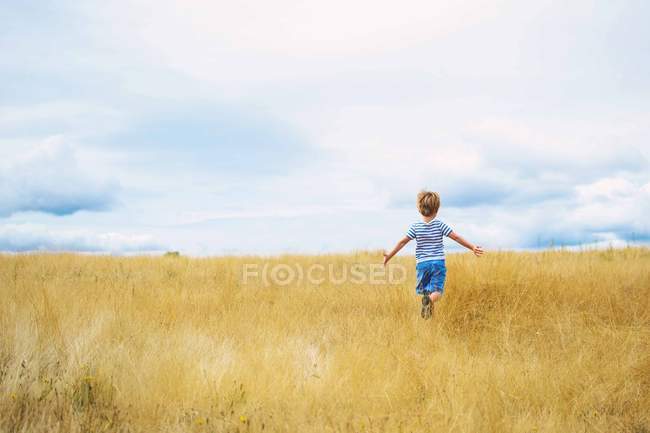 Pequeno menino correndo através do campo sob céu nublado — Fotografia de Stock