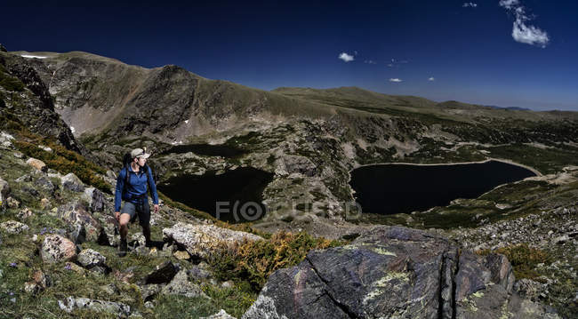 Hombre de pie entre las rocas en la ladera de la montaña con tres lagos en el fondo, EE.UU., Colorado, Montañas Rocosas - foto de stock