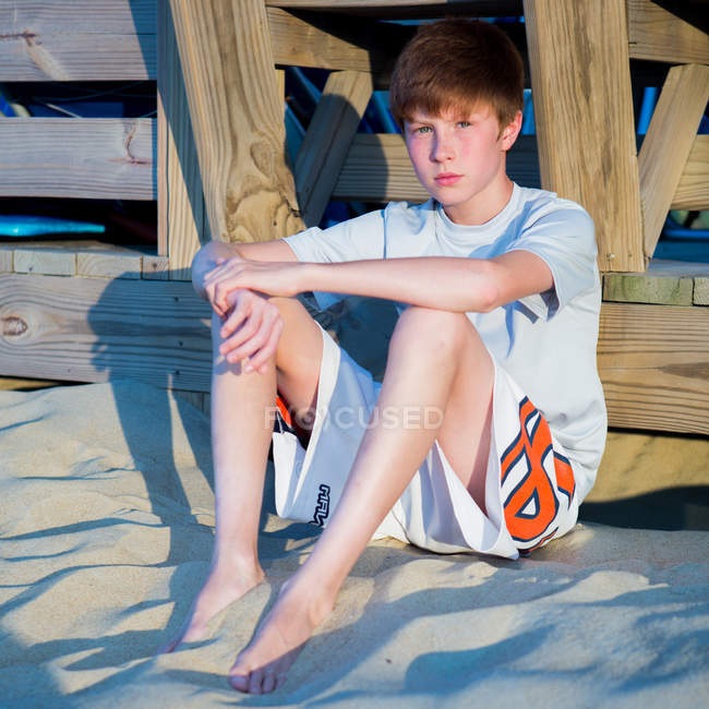 Мальчик сидит на песчаном пляже и прислоняется к набережной — стоковое фото