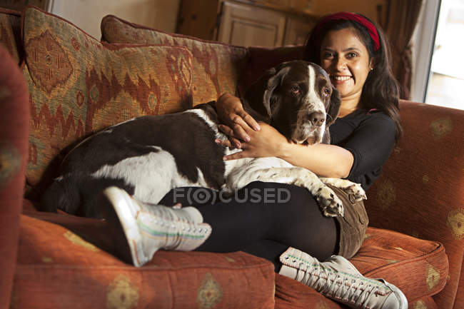 Женщина обнимает старого пса дома на диване — стоковое фото