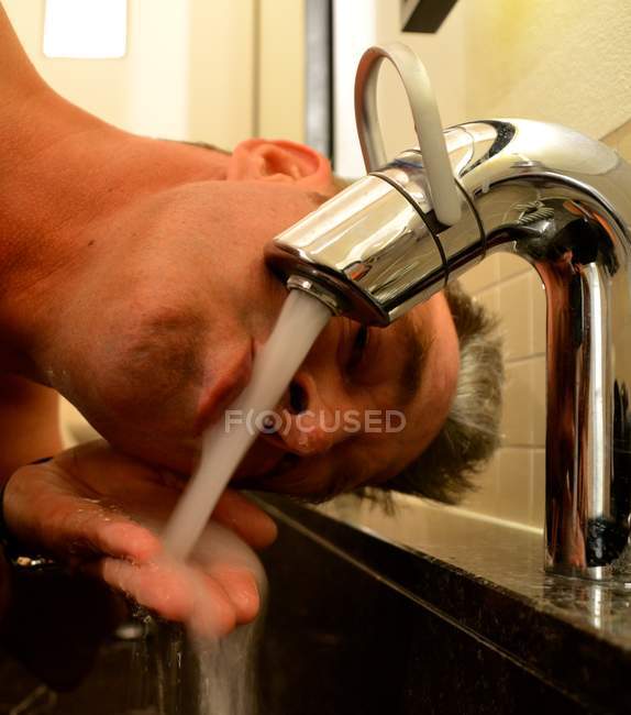 Крупным планом зрелого человека питьевая вода из крана — стоковое фото
