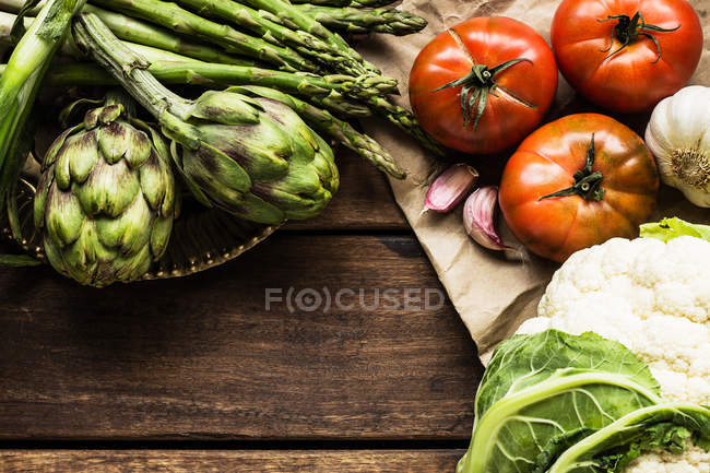 Coliflor, alcachofas, espárragos, ajo y tomates sobre mesa de madera - foto de stock
