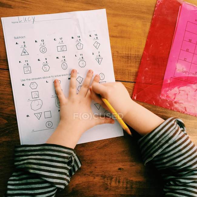 Крупним планом вид зверху руки маленької дівчинки робить її домашнє завдання — стокове фото