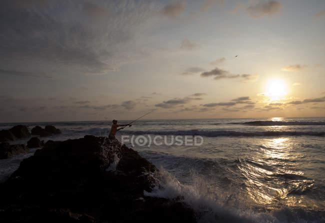 Ecuador, L'uomo pesca sulla roccia nell'Oceano Pacifico al tramonto — Foto stock