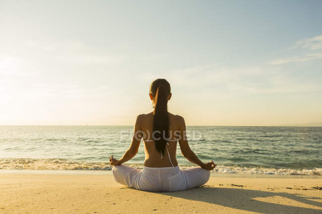 Вид ззаду жінки, що медитує на піщаному пляжі — стокове фото