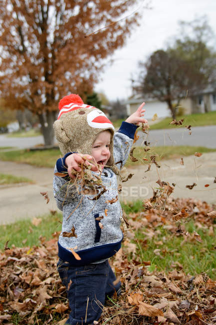 Хлопчик у смішному капелюсі кидає листя в парк — стокове фото