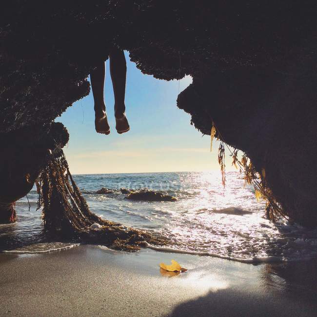 Abgeschnittenes Bild von Personenbeinen, die vor dem Höhleneingang am Strand hängen — Stockfoto