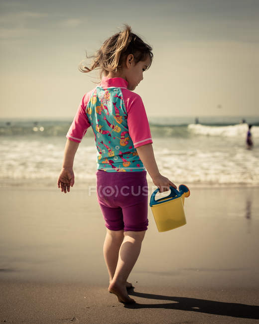 Girl walking along beach with toy watering can — Stock Photo