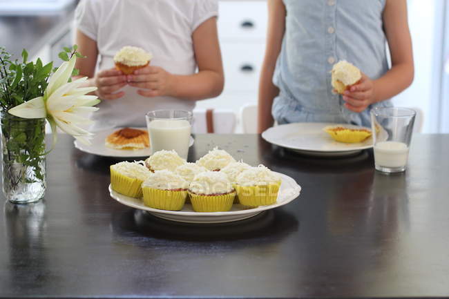 Частичный вид маленьких девочек с вкусными кексами на кухне — стоковое фото