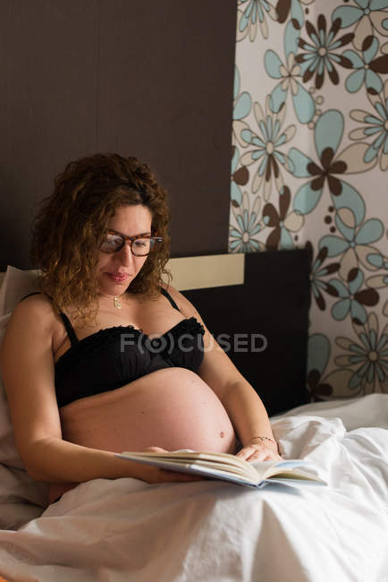 Беременная женщина читает книгу в спальне — стоковое фото