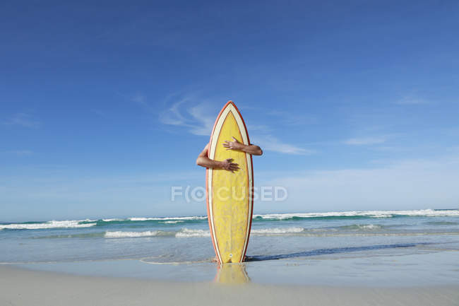 Man embracing surfboard on sandy beach — Stock Photo