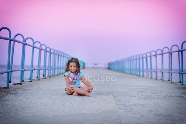 Портрет дівчини, що сидить на пірсі на заході сонця — стокове фото
