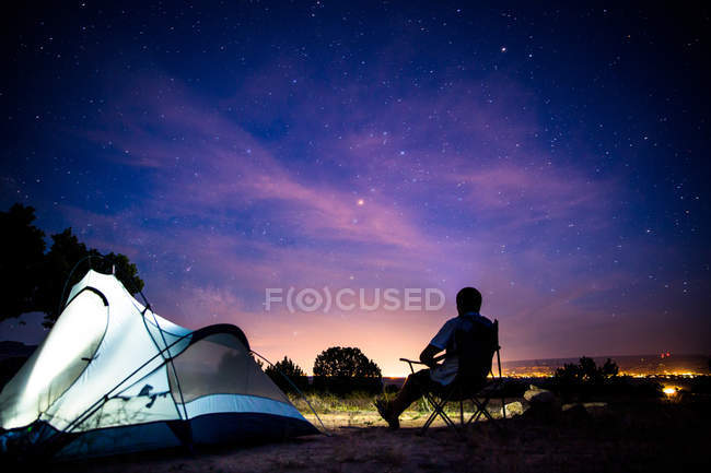Мужчина, сидящий около освещенной палатки ночью — стоковое фото