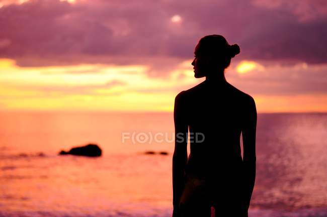 Silhouette d'une femme debout à la plage au coucher du soleil — Photo de stock