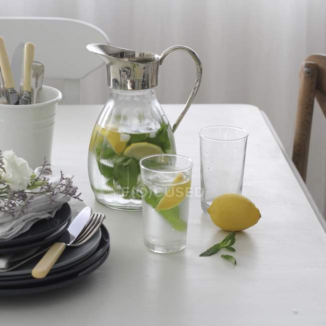 Jarra y vaso de agua infundido con limón fresco y menta - foto de stock