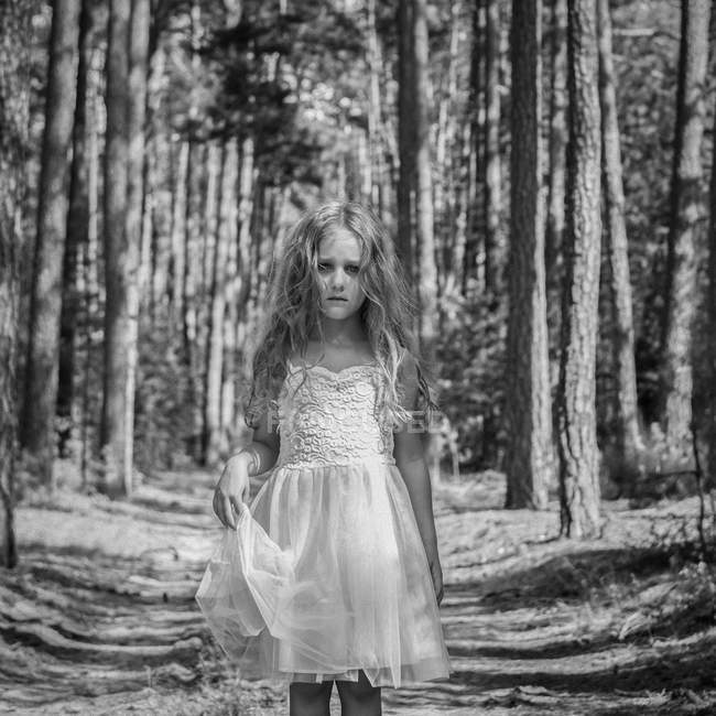 Retrato de niña triste vestida de blanco vestido festivo de pie en el bosque - foto de stock