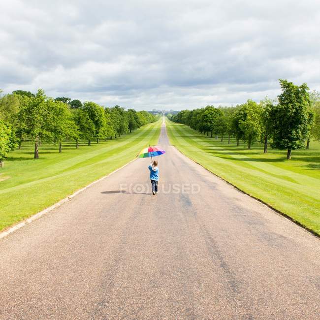 Boy walking with colorful umbrella along road in countryside — Stock Photo