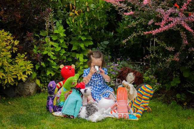 Menina tendo festa de chá com brinquedos no gramado — Fotografia de Stock