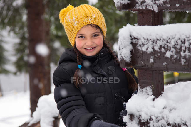 Menina sorridente usando chapéu amarelo de pé no inverno — Fotografia de Stock