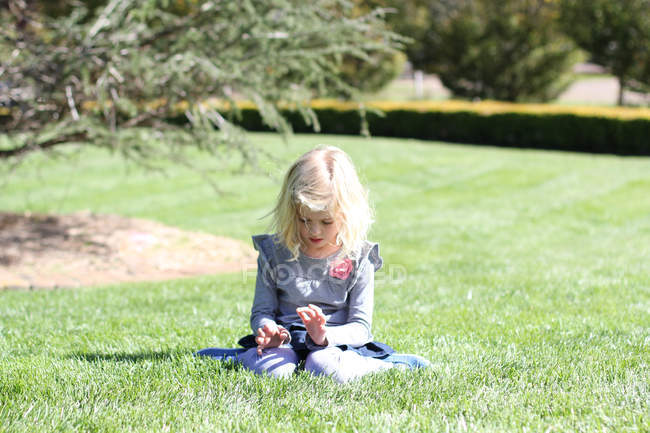 Nachdenkliches blondes kleines Mädchen auf Gras sitzend — Stockfoto
