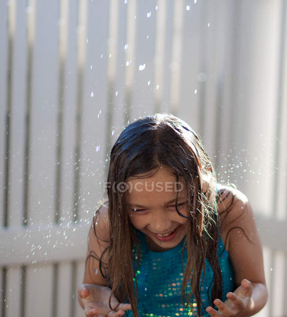 Sonriente niña bajo spray de agua al aire libre - foto de stock