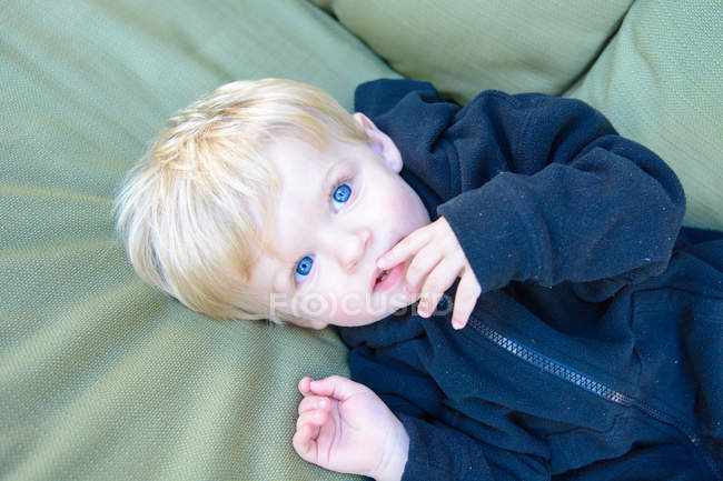 Petit garçon blond aux yeux bleus couché sur le canapé — Photo de stock